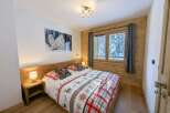 Cozy bedroom with wooden walls and floors, featuring a double bed with festive bedding and a large window offering stunning views of a snow-covered landscape.