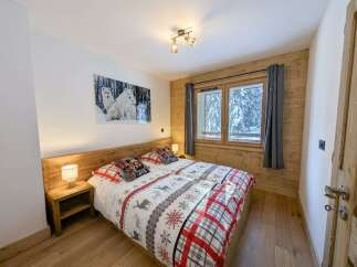 Cozy bedroom with wooden walls and floors, featuring a double bed with festive bedding and a large window offering stunning views of a snow-covered landscape.