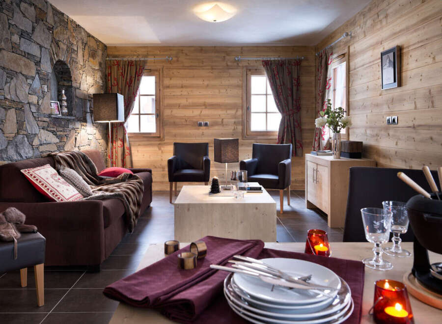 This stunning chalet boasts a cozy living area with a plush brown sofa, two comfortable armchairs, and a rustic wooden coffee table.