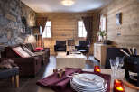 This stunning chalet boasts a cozy living area with a plush brown sofa, two comfortable armchairs, and a rustic wooden coffee table.