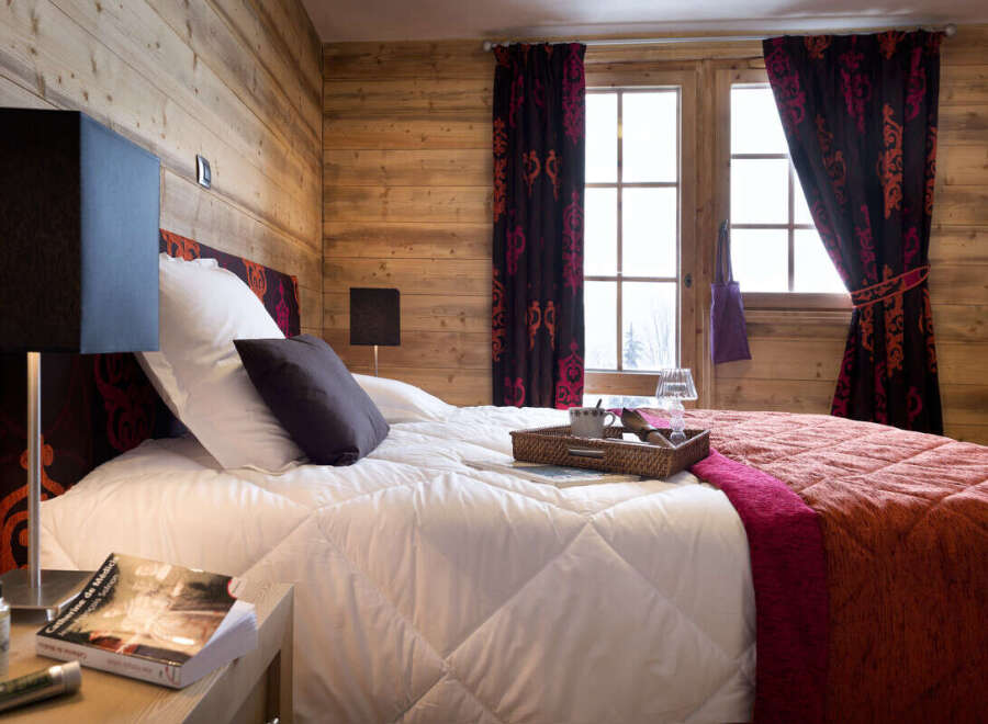 Cozy bedroom with wooden walls and a comfortable bed, featuring a tray with coffee and a book on the nightstand.