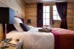 Cozy bedroom with wooden walls and a comfortable bed, featuring a tray with coffee and a book on the nightstand.