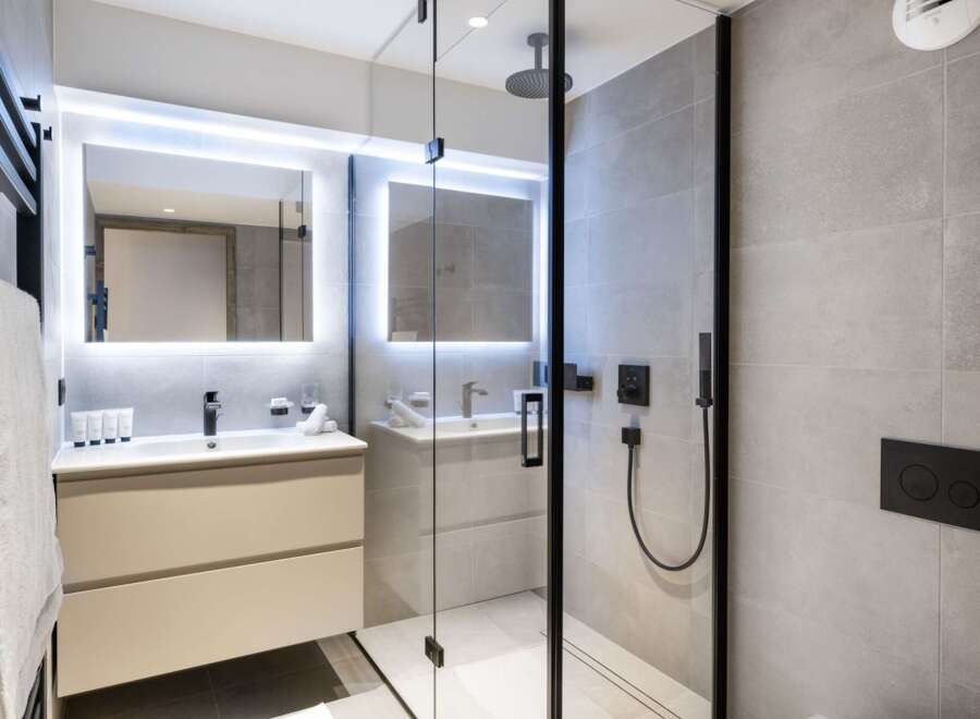 This modern bathroom boasts a spacious walk-in shower with a rainfall shower head, sleek black fixtures, and elegant gray tile.