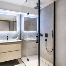 This modern bathroom boasts a spacious walk-in shower with a rainfall shower head, sleek black fixtures, and elegant gray tile.