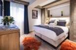 This luxurious bedroom boasts a king-size bed with plush bedding, complemented by a stylish wooden headboard and built-in storage.