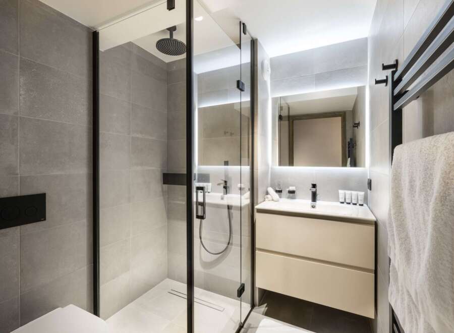 This modern bathroom boasts a sleek glass shower enclosure with a rainfall shower head, complemented by a minimalist vanity with ample storage.