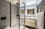 This modern bathroom boasts a sleek glass shower enclosure with a rainfall shower head, complemented by a minimalist vanity with ample storage.