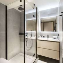 This modern bathroom boasts a sleek glass shower enclosure with a rainfall shower head, complemented by a minimalist vanity with ample storage.