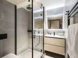 This modern bathroom boasts a sleek glass shower enclosure with a rainfall shower head, complemented by a minimalist vanity with ample storage.