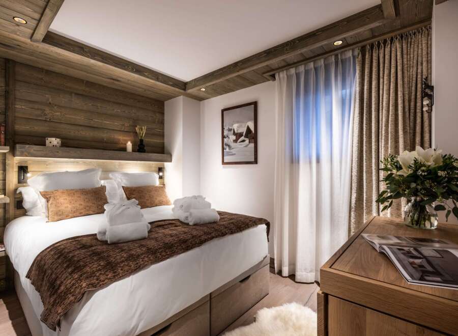 This luxurious bedroom boasts a king-size bed with plush bedding and a cozy brown throw, complemented by built-in wooden shelving and lighting.