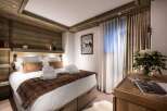 This luxurious bedroom boasts a king-size bed with plush bedding and a cozy brown throw, complemented by built-in wooden shelving and lighting.
