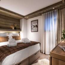 This luxurious bedroom boasts a king-size bed with plush bedding and a cozy brown throw, complemented by built-in wooden shelving and lighting.
