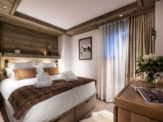 This luxurious bedroom boasts a king-size bed with plush bedding and a cozy brown throw, complemented by built-in wooden shelving and lighting.