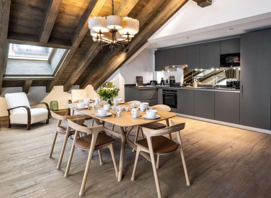 This stunning chalet boasts a spacious open-plan living area with a rustic wooden beamed ceiling and large skylights, creating a bright and airy atmosphere.