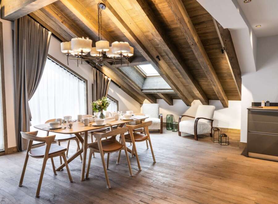 This stunning chalet boasts a spacious open-plan living area with exposed wooden beams and a large dining table perfect for family gatherings.