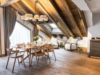 This stunning chalet boasts a spacious open-plan living area with exposed wooden beams and a large dining table perfect for family gatherings.
