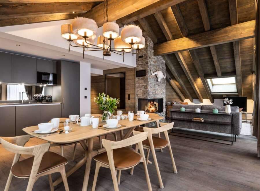 This stunning chalet boasts a spacious open-plan living area with a rustic wooden beamed ceiling and a cozy fireplace, perfect for relaxing after a day on the slopes.