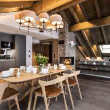 This stunning chalet boasts a spacious open-plan living area with a rustic wooden beamed ceiling and a cozy fireplace, perfect for relaxing after a day on the slopes.