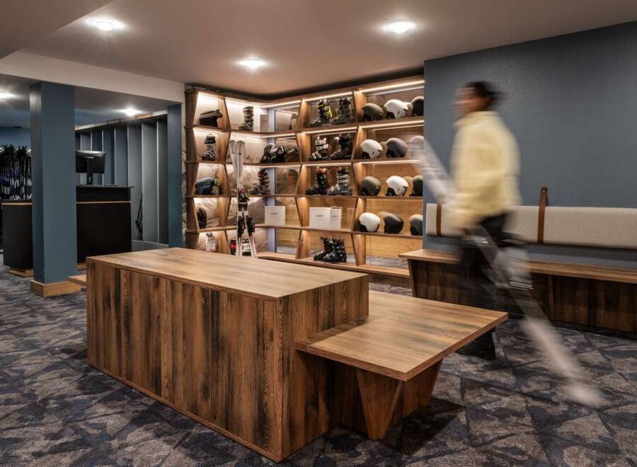 This stunning ski rental shop boasts a modern design with rustic wooden furniture and sleek shelving units showcasing an array of skis, boots, and helmets.