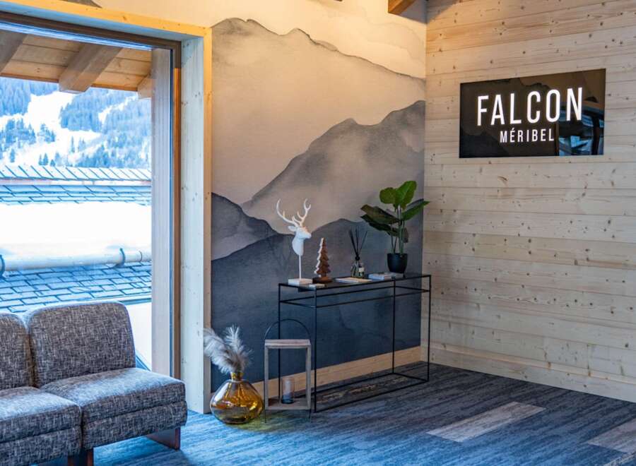 This stunning Méribel chalet boasts a stylish interior with a mountain-view window, a cozy seating area, and a modern console table.
