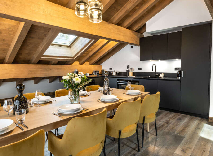 This stunning chalet boasts a spacious open-plan dining area with a large wooden table and mustard yellow velvet chairs, perfect for family gatherings.