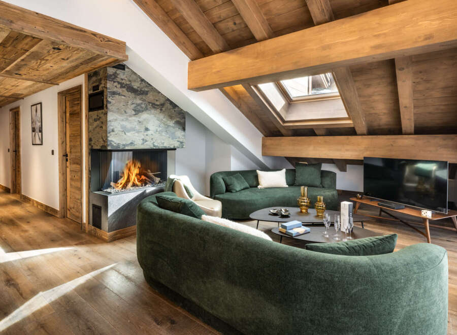 This stunning chalet boasts a spacious open-plan living area with a cozy fireplace, plush green sofas, and large windows offering ample natural light.