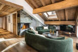 This stunning chalet boasts a spacious open-plan living area with a cozy fireplace, plush green sofas, and large windows offering ample natural light.