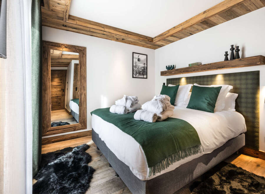 This luxurious bedroom boasts a king-size bed with plush bedding, a cozy green throw, and a sheepskin rug.