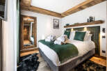 This luxurious bedroom boasts a king-size bed with plush bedding, a cozy green throw, and a sheepskin rug.