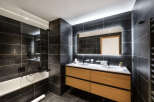 This luxurious bathroom boasts a sleek, modern design with dark gray tile, a spacious double vanity with light wood cabinets, and a frameless glass shower enclosure.