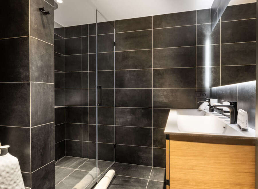 Modern bathroom with dark gray tiles, a glass shower enclosure, and a light wood vanity.