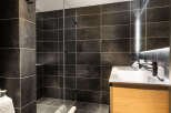 Modern bathroom with dark gray tiles, a glass shower enclosure, and a light wood vanity.