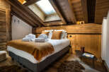 Cozy chalet bedroom with wooden beams, skylights, and a plush bed dressed in warm-toned textiles.