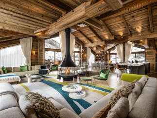 This luxurious chalet boasts a spacious open-plan living area with a stunning fireplace as the centerpiece, surrounded by comfortable seating and large windows offering breathtaking mountain views.