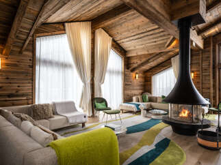 This luxurious chalet boasts a stunning open-plan living area with floor-to-ceiling windows offering breathtaking views, a cozy fireplace as the centerpiece, and plush seating arrangements perfect for relaxation.