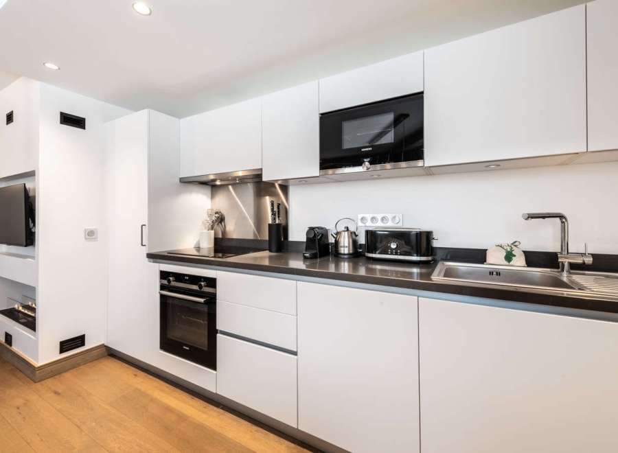 Modern kitchen with white cabinets, dark countertops, and integrated appliances including a microwave, oven, and cooktop.