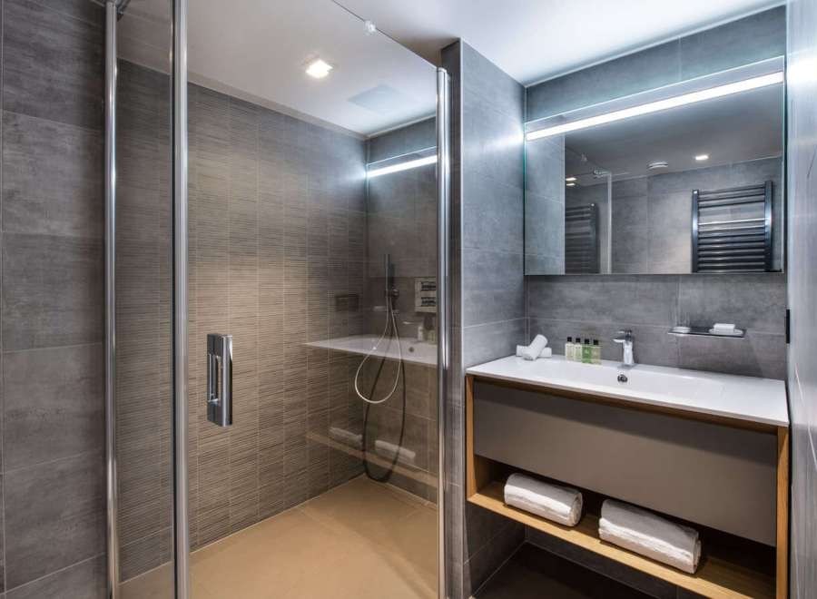 Modern bathroom with a walk-in shower, sleek gray tile, and a floating vanity with integrated shelving.