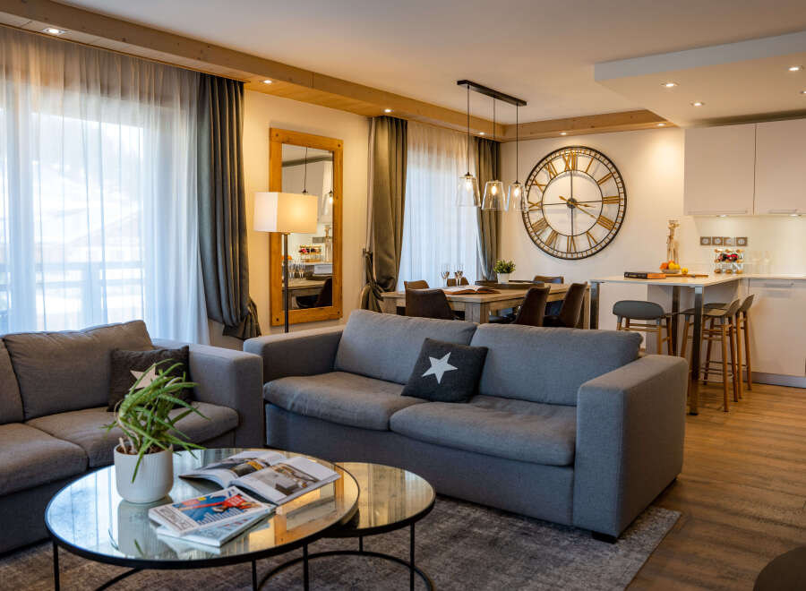 This stunning apartment boasts an open-plan living area with comfortable grey sofas, a stylish glass coffee table, and large windows offering ample natural light.
