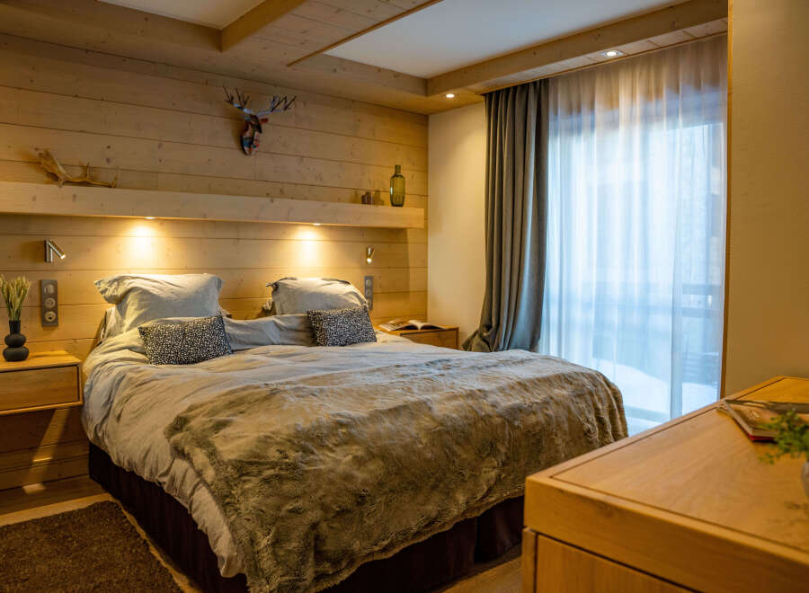 Cozy bedroom with wooden walls and a plush bed, featuring a faux fur throw and decorative pillows.