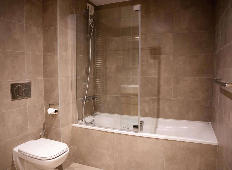 This modern bathroom boasts a sleek, built-in bathtub with a glass shower enclosure, complemented by contemporary chrome fixtures.