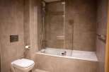 This modern bathroom boasts a sleek, built-in bathtub with a glass shower enclosure, complemented by contemporary chrome fixtures.