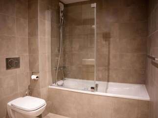 This modern bathroom boasts a sleek, built-in bathtub with a glass shower enclosure, complemented by contemporary chrome fixtures.
