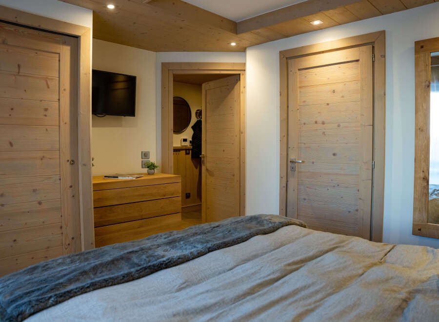 This stunning bedroom boasts a cozy and elegant design, featuring a plush bed with a soft throw, wooden doors and floors, and recessed lighting.