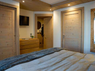 This stunning bedroom boasts a cozy and elegant design, featuring a plush bed with a soft throw, wooden doors and floors, and recessed lighting.