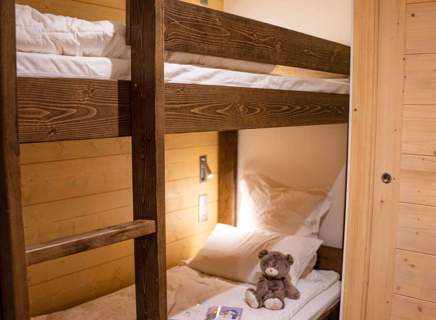 Cozy bunk beds with plush bedding and a teddy bear add a touch of whimsy to this charming wooden-paneled room.