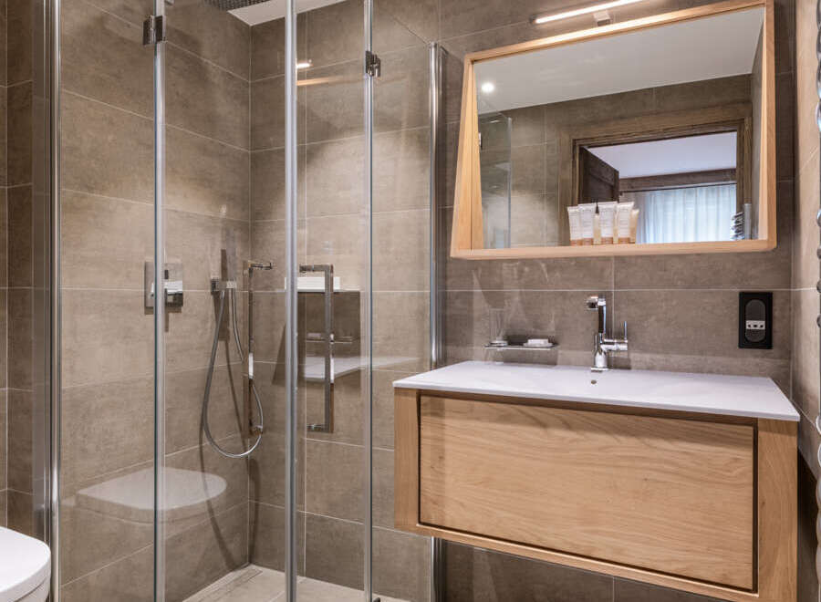 This luxurious bathroom boasts a spacious walk-in shower with glass enclosure, a sleek wooden vanity with integrated sink, and modern fixtures.