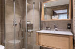 This luxurious bathroom boasts a spacious walk-in shower with glass enclosure, a sleek wooden vanity with integrated sink, and modern fixtures.