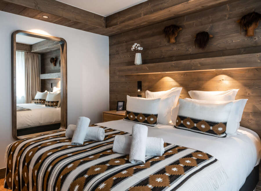 Cozy bedroom with a wooden wall and a comfortable bed featuring a patterned throw blanket.