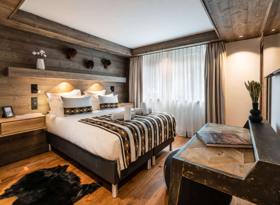This stunning bedroom boasts a cozy, rustic-chic design with wood paneling, a plush bed dressed in rich textiles, and a stylish writing desk.