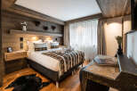 This stunning bedroom boasts a cozy, rustic-chic design with wood paneling, a plush bed dressed in rich textiles, and a stylish writing desk.